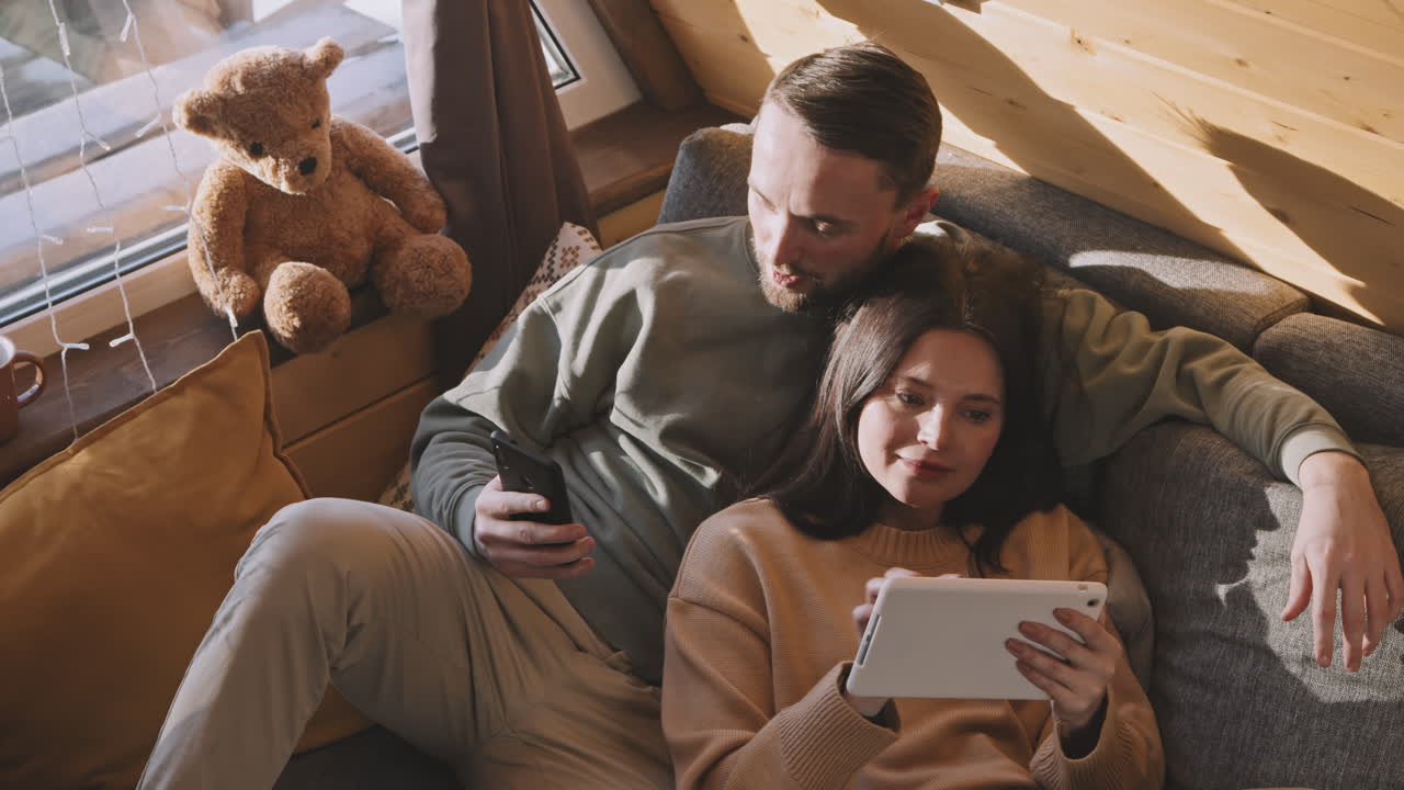 Couple Using Gadgets and Relaxing on Couch in Cabin