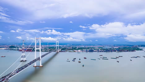 Vista-De-Pájaro-De-Importante-Construcción-De-Infraestructura-Cruce-De-Puentes-De-Autopistas-Marítimas-Con-Tráfico-En-Hora-Punta-En-El-Este-Cruza-La-Bahía-Bajo-Un-Cielo-Azul