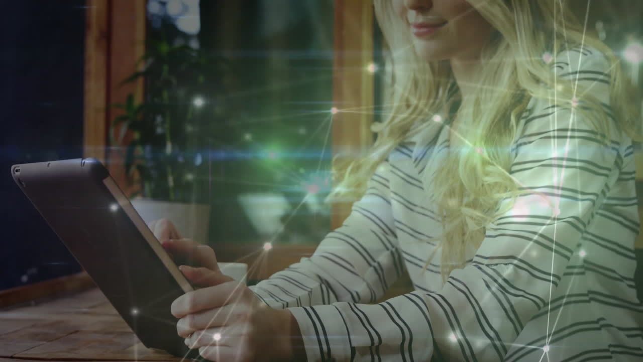 Woman sitting at wooden table using tablet in tech workspace, with green network lines overlaying