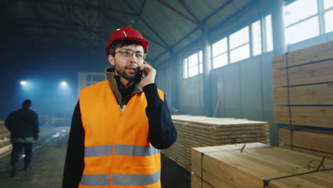 engineer in a helmet walks through a warehouse of building materials and talks on the phone 1