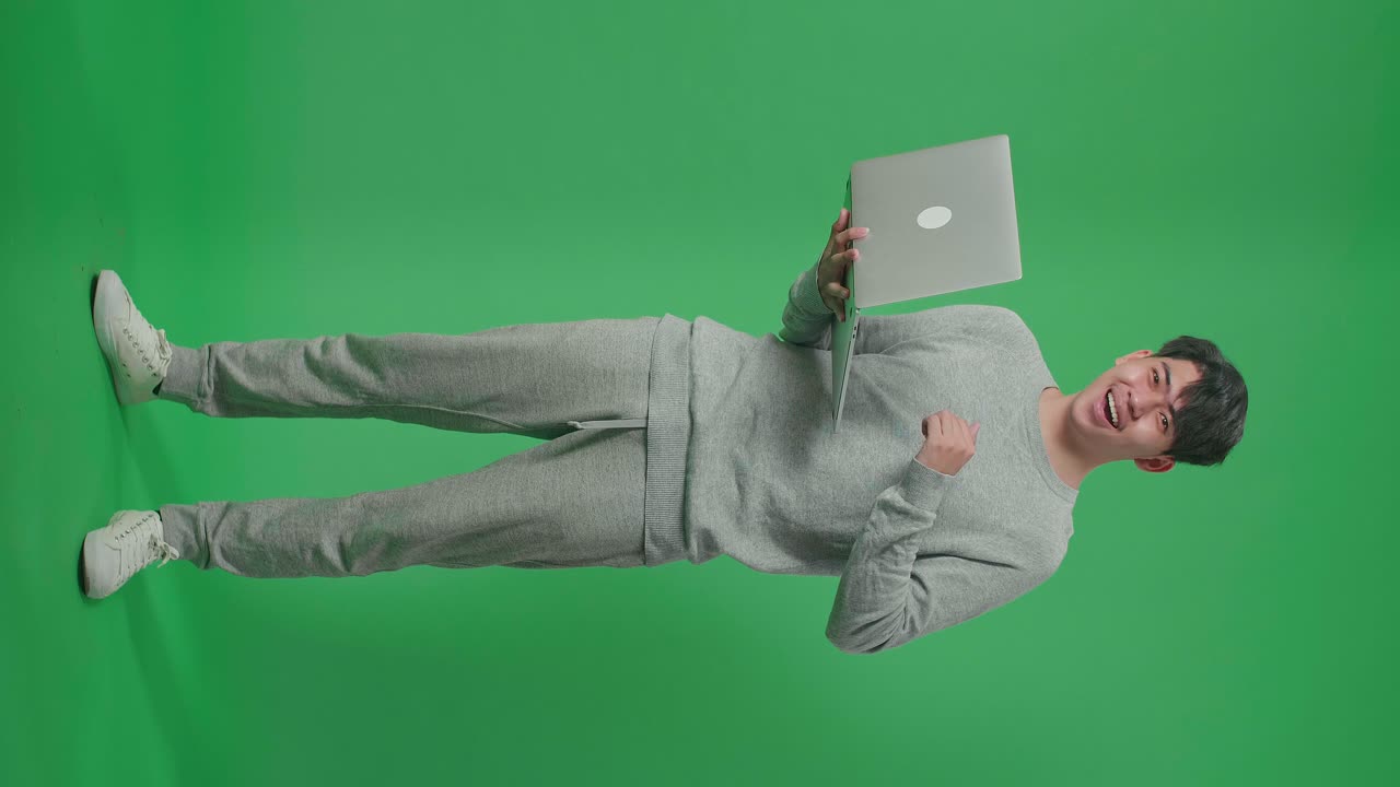 cuerpo lleno de hombre asiático sonriente diciendo wow mientras usa la computadora en el fondo de la pantalla verde