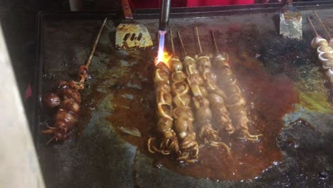 process of making and barbequing of squid skewer, it's seasoned with tomato sauce and chili paste