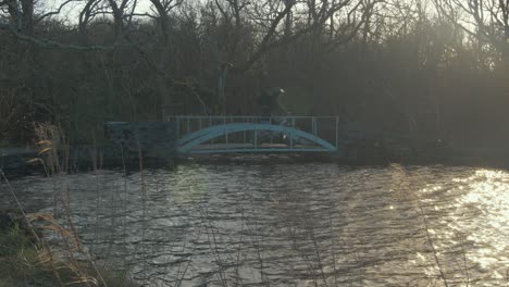 Man-cycling-along-forest-path-cycles-across-bridge-by-river