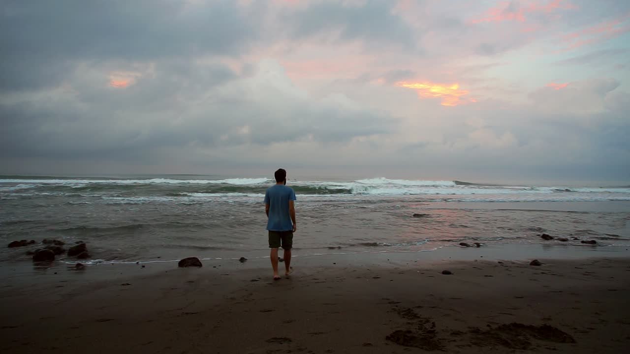 A person walks along the shore, gazing at the waves during a calm moment at sunset