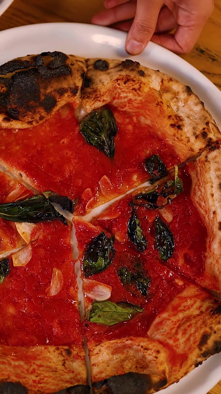 Vista dall'alto di mani che tagliano una pizza sottile con salsa di pomodoro e foglie di basilico