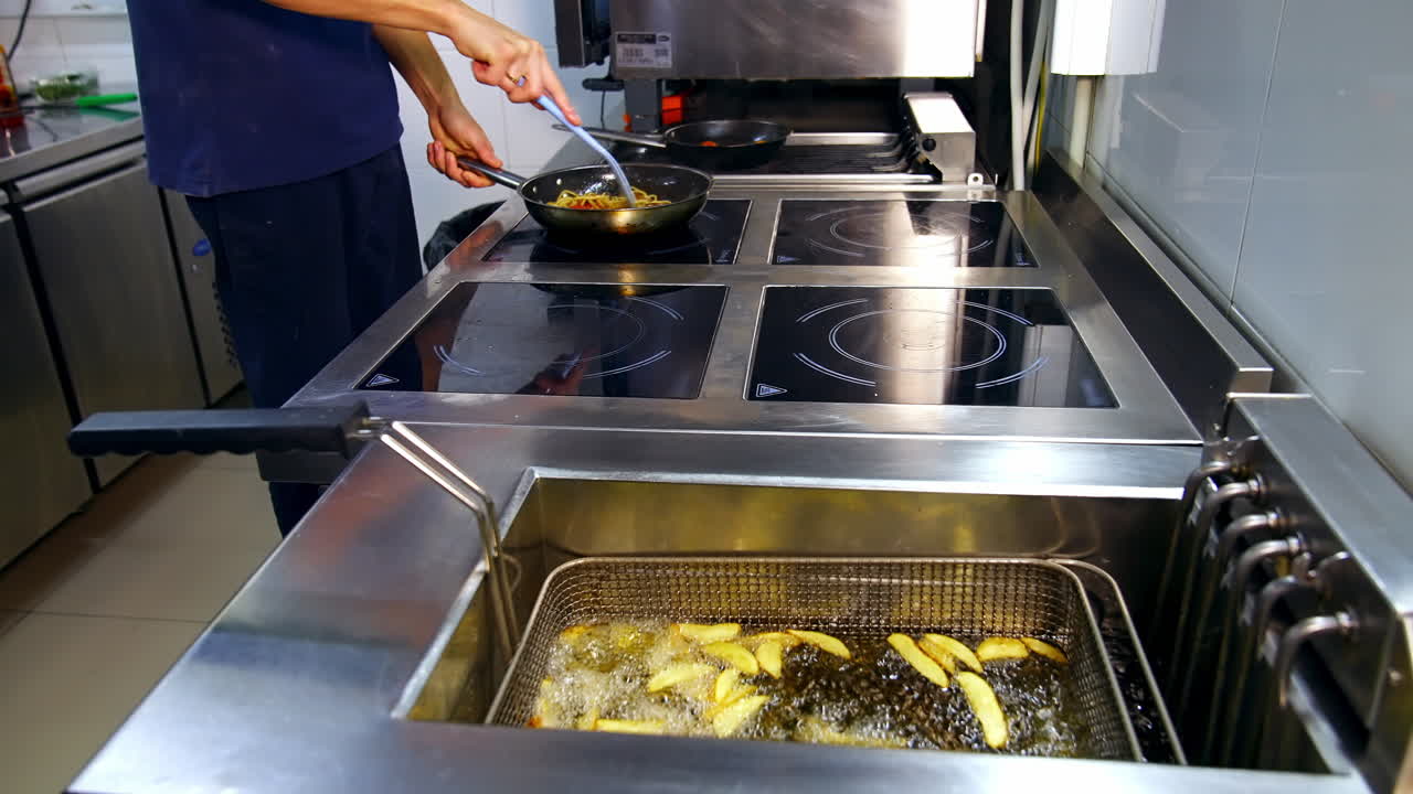 Deep fryer in the kitchen restaurant. Chef is cooking food in the frying pan. Crispy potatoes frying in hot boiled oil. Delicious meals.