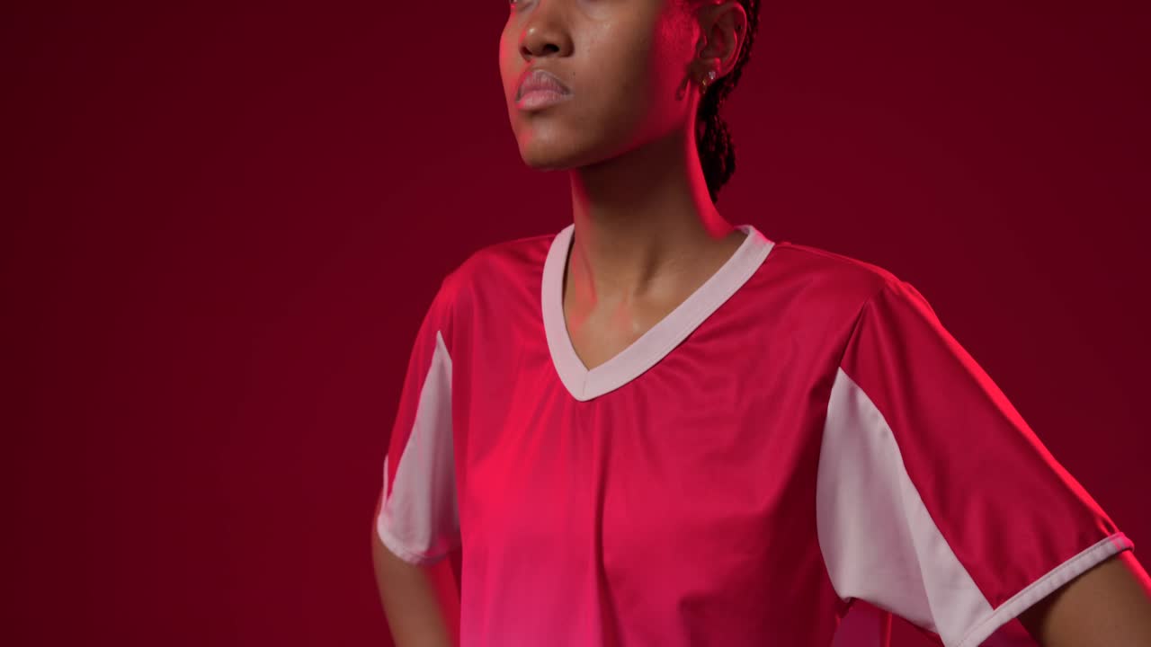 Cámara paneando hacia arriba a una mujer afroamericana con camiseta roja, levantando la cabeza y revelando su rostro en el estudio.