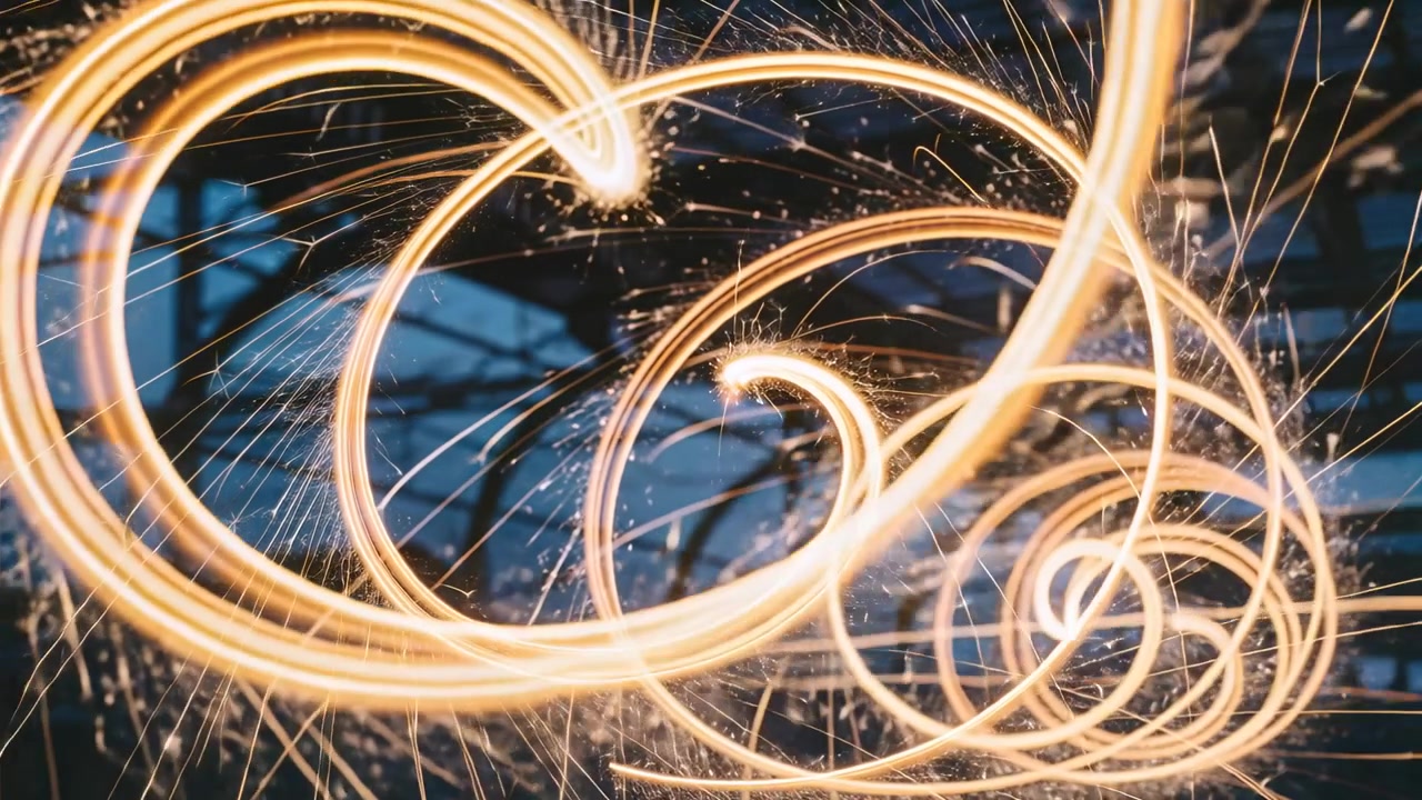 Stellina pirotecnica che ruota, iniziando un movimento circolare tra raggi blu scuro, creando spirali dorate sovrapposte.
