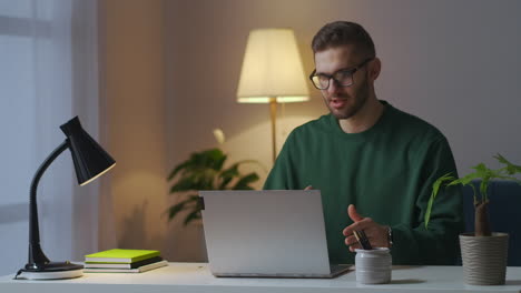 Der-Junge-Lehrer-Hält-Online-Eine-Vorlesung-Und-Spricht-Per-Webkamera-Vor-Dem-Publikum,-Das-Abends-Von-Zu-Hause-Aus-Arbeitet.-Mittleres-Porträt-Eines-Intelligenten-Mannes