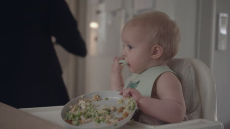 toddler sitting in high chair eating solids from plate