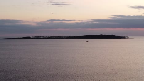 Vista-Panorámica-Aérea-De-La-Silueta-Del-Barco-Distante-Al-Atardecer-Con-La-Isla-Gorriti-En-El-Fondo