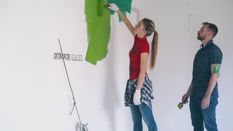 woman paints wall with grass green husband stands in room