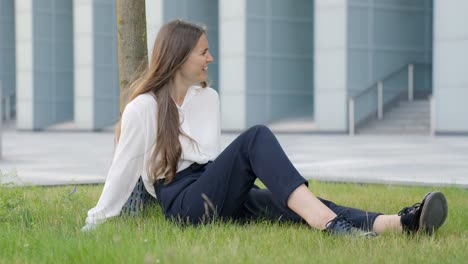 girl sitting relaxed on grass in front of building and having conversation