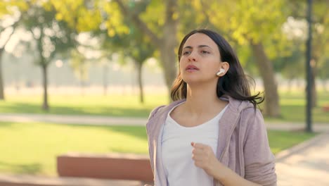 niña india corriendo con auriculares en un parque por la mañana