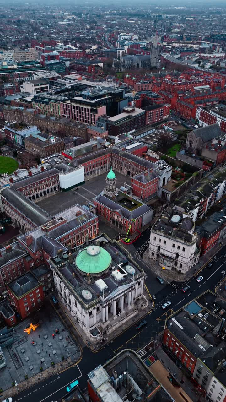 Portret lotniczy z drona, przesuwający się w kierunku zamku w Dublinie w centrum miasta w Irlandii w zimowy dzień, pochmurny z chmurami w południe, z ruchliwymi drogami poniżej, z samochodami i turystami spacerującymi na dole