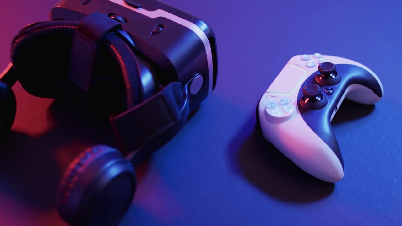 Video of close up of video game pad controller and vr headset with copy space on neon background