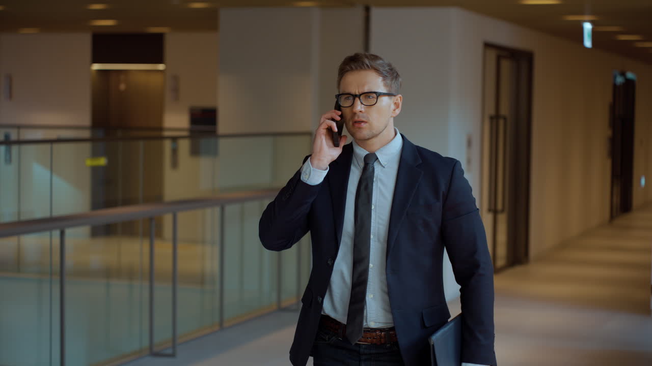 una toma lateral de un hombre de negocios hablando en su teléfono inteligente mientras camina por el pasillo de la oficina.
