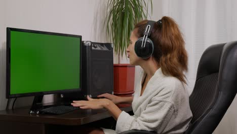 a woman is watching tv with a green screen and listening to music on headphones.