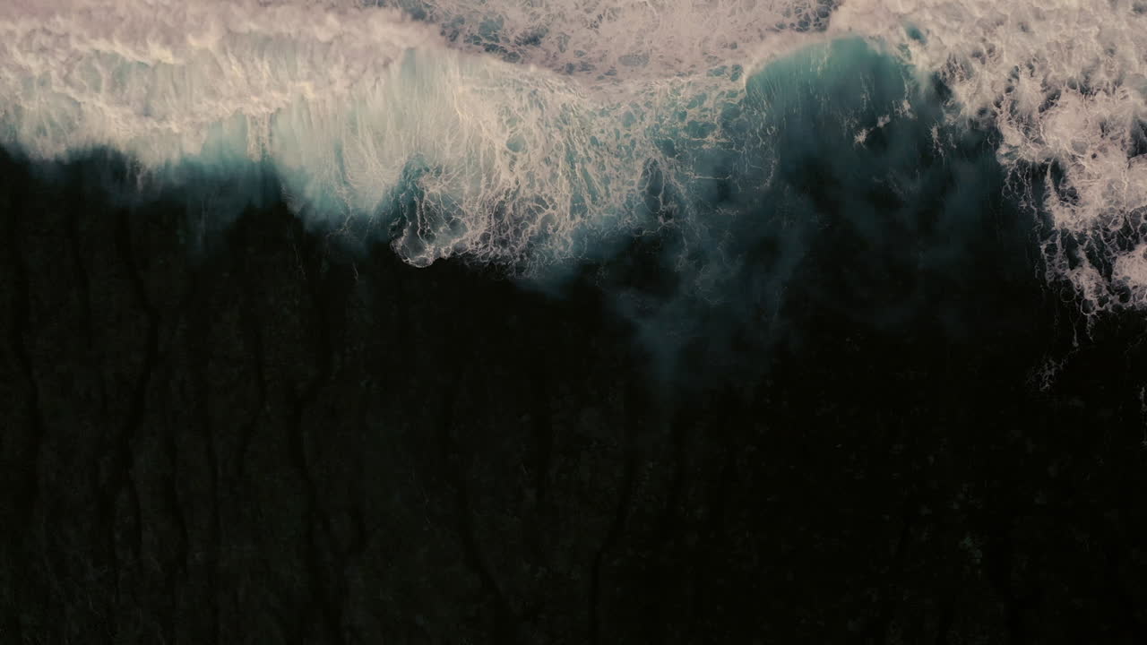 Aerial birds eye view of dramatic dark moody ocean water with white foaming waves breaking