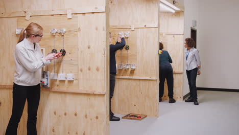 female tutor with trainee electricians in workshop studying for apprenticeship at college