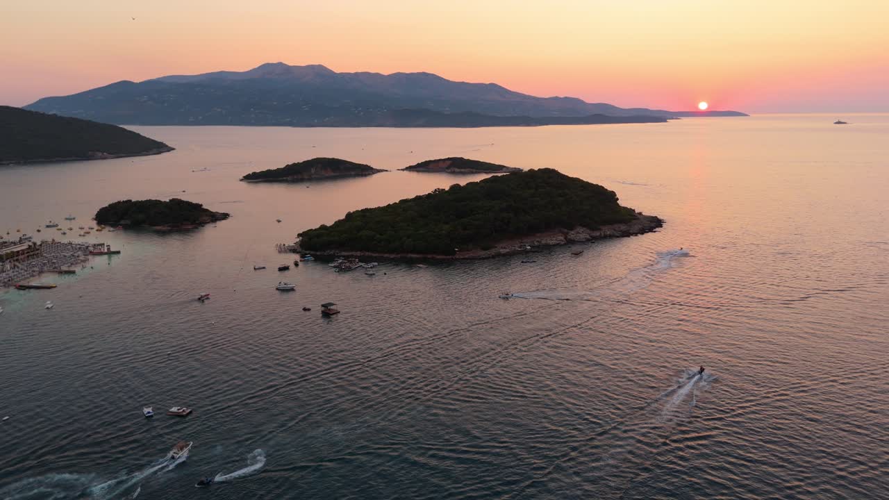 Boats sailing around small islands in the golden hour sunset near Ksamil, Albania with mountains in view