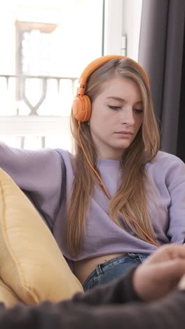 young couple relaxing and sitting on couch at home while reading a book and listening music with headphones