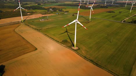 aerial shot of the wind turbines working in a wind farm generating green electric energy on a wide green field on a sunny day, use of renewable resources of energy, 4k