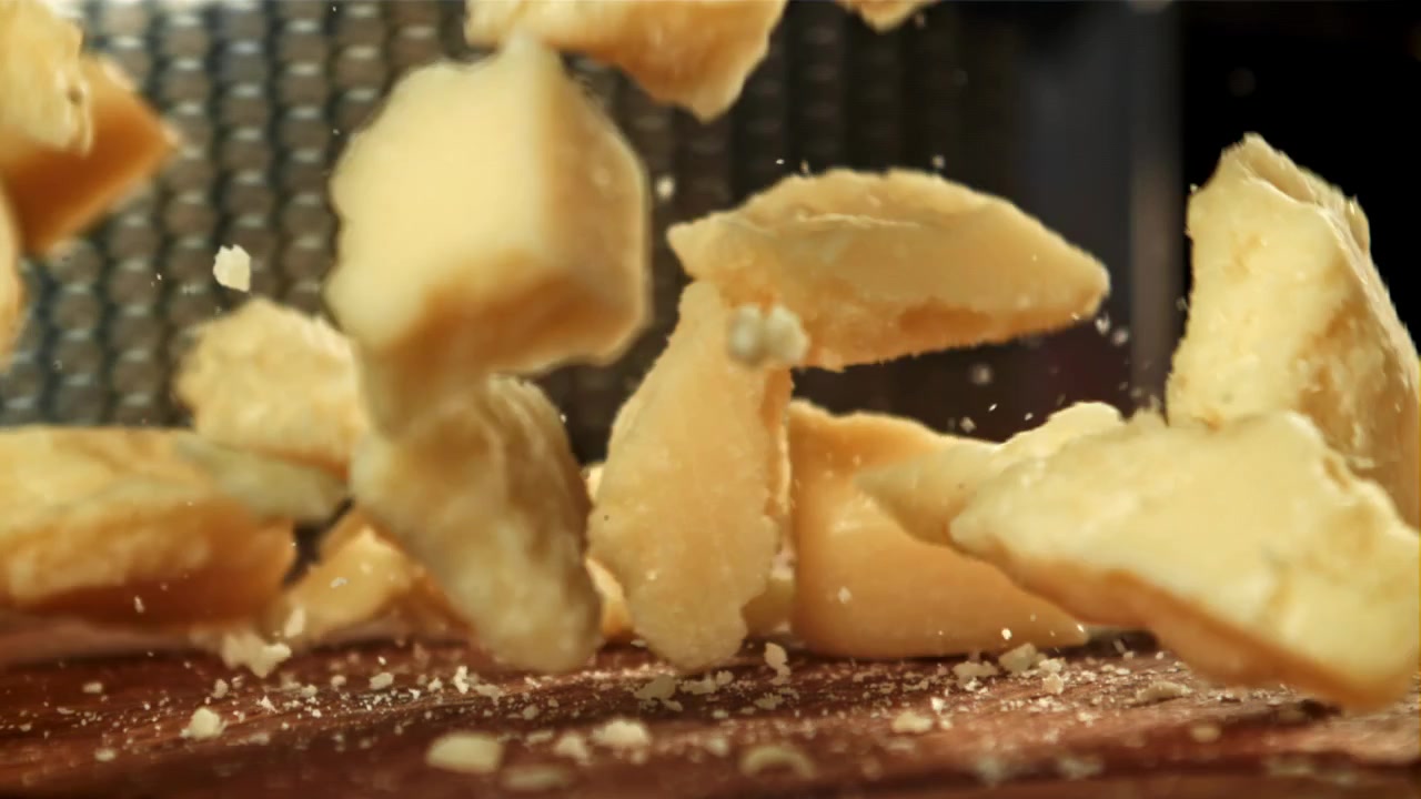 Pezzi di Parmigiano che cadono al rallentatore su una superficie di legno