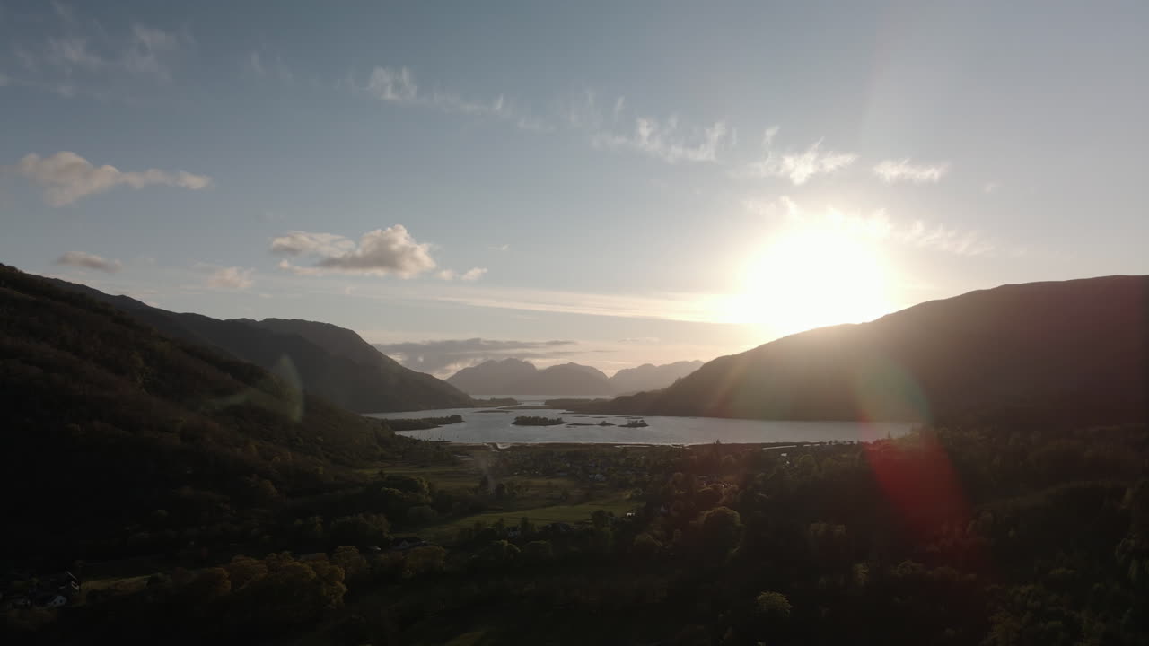 Imagem de drone da vila de Glencoe e Loch Leven numa noite de verão, com as terras altas ao fundo e reflexo solar.