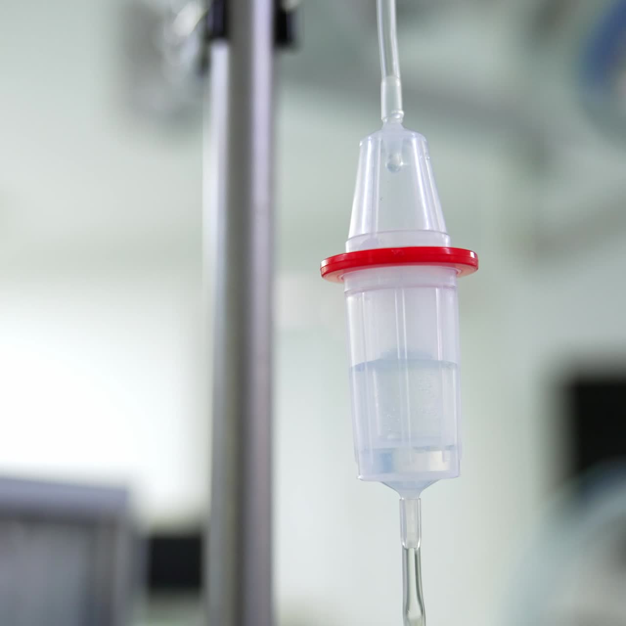 Liquid dripping in the drop counter hanging in the surgery room. Close up. Blurred backdrop