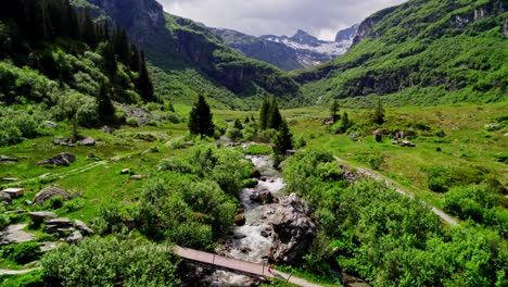 Carefree-young-woman-dancing-across-alpine-stream-on-bridge,-aerial