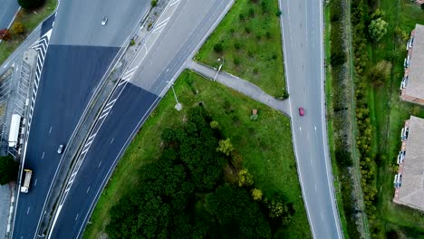 aerial view over motorway exit in france. only homes and grass fields around roads. cars and trucks driving on the roads.