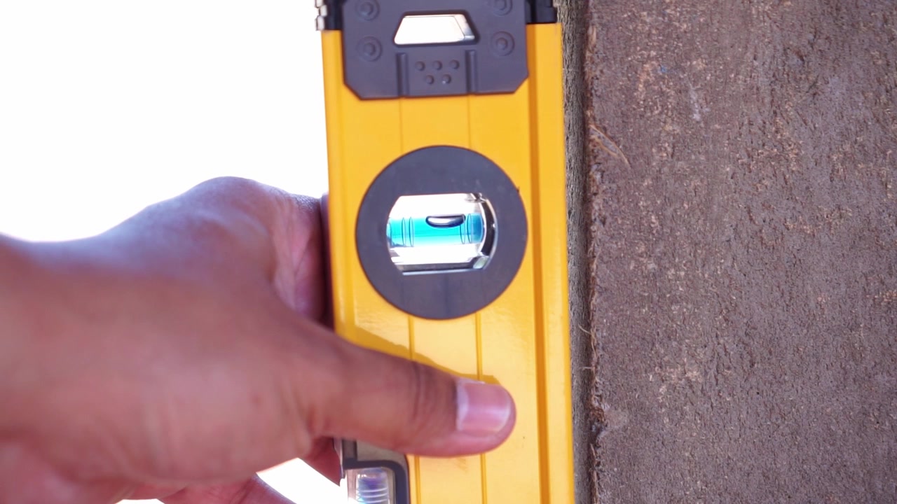 hand holding yellow spirit level against pillar, construction tool, precision measurement concept.