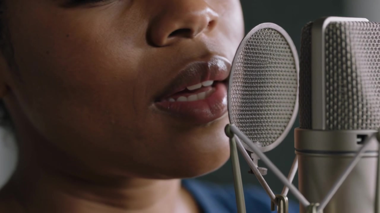 Cueing studio vocalist in blue top singing into condenser mic hand nudging pop filter, copy space