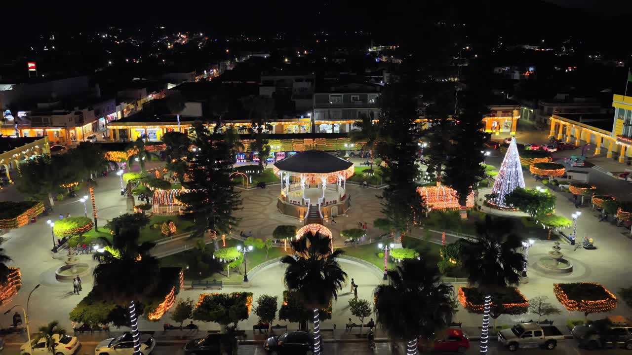 Vista aérea de la plaza central de un pequeño pueblo mexicano, decorada para Navidad con una glorieta muy iluminada y un gran árbol de Navidad cónico.