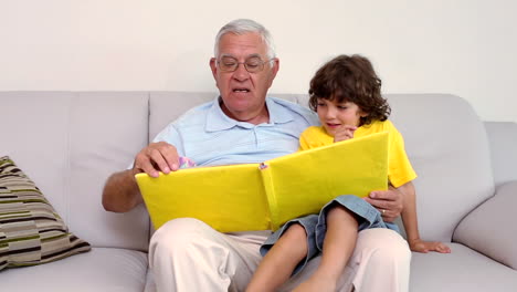 Senior-man-sitting-on-couch-with-his-grandson-looking-at-photo-album