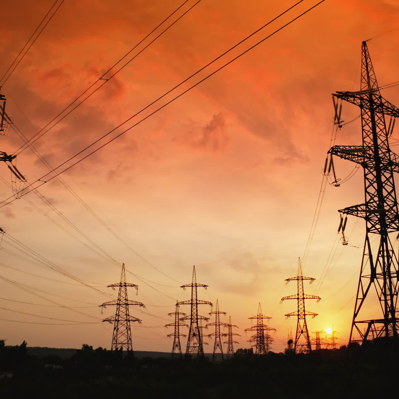 Tall electric towers at sunset. High voltage electric line distribute electricity through cables. Distribution station with metal pylons in the evening. Slow motion