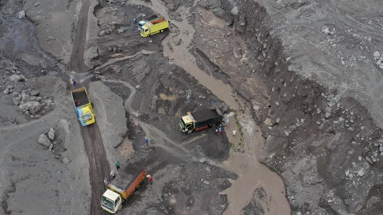 vista aérea de camiones volquete llenos de arena volcánica negra tirando de un arroyo, java oriental, indonesia