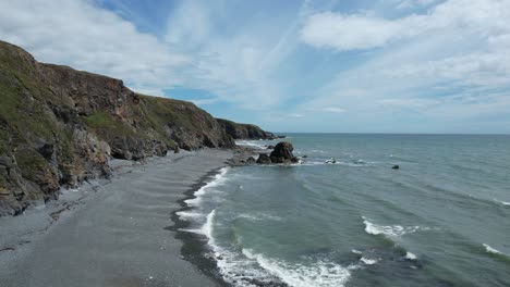 Establishing-drone-shot-moving-along-the-coast-and-shingle-beach-at-low-tide-at-Tankardstown-Beach-Copper-Coast-Waterford-Ireland-on-a-blustery-summer-day