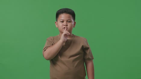 스튜디오에서 녹색 스크린 배경에서 침 제스처를 보여주는 아시아 소년