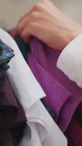 primer plano de la mano femenina seleccionando tela púrpura de un estante de ropa en una tienda minorista, mostrando una experiencia de compra reflexiva, colores vibrantes y atención a los detalles en un entorno de moda moderno