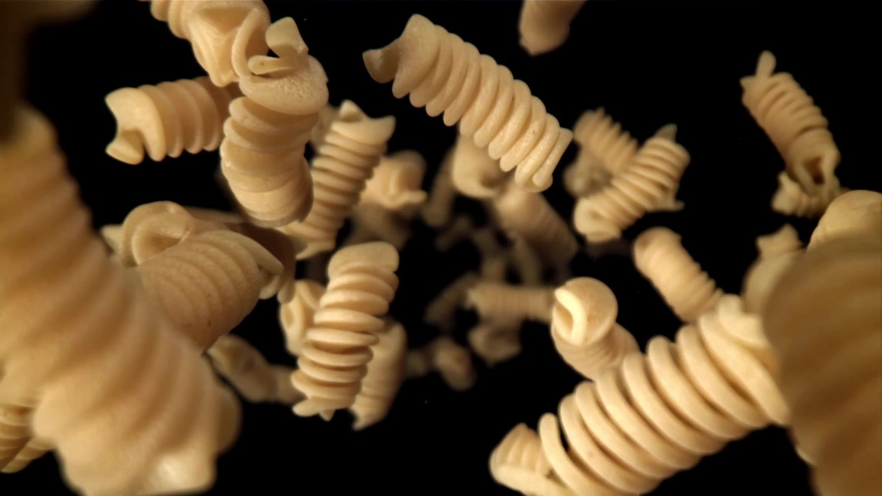 Pasta fusilli cruda che cade al rallentatore su sfondo nero
