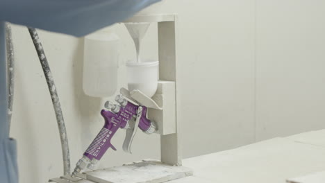 laborer pours white paint into a airbrush tool preparing to work in a spray booth slow motion