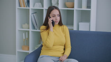 happy mature woman with talking on smartphone while sitting at living room with modern interior. concept of technology and relaxation.