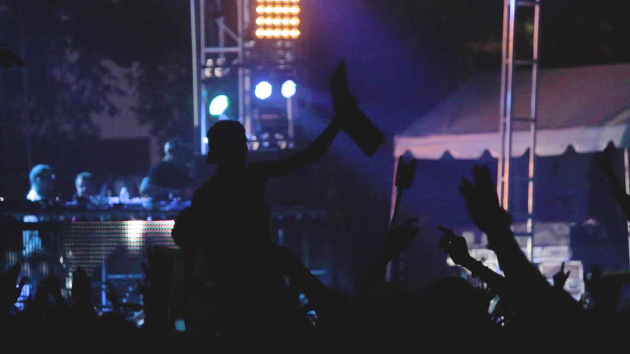 Un uomo festeggia con energia a un festival di musica dal vivo. Salta su e giù lanciando le braccia in aria con passione per la musica. Luci e colori e migliaia di persone ballano al ritmo del musicista.