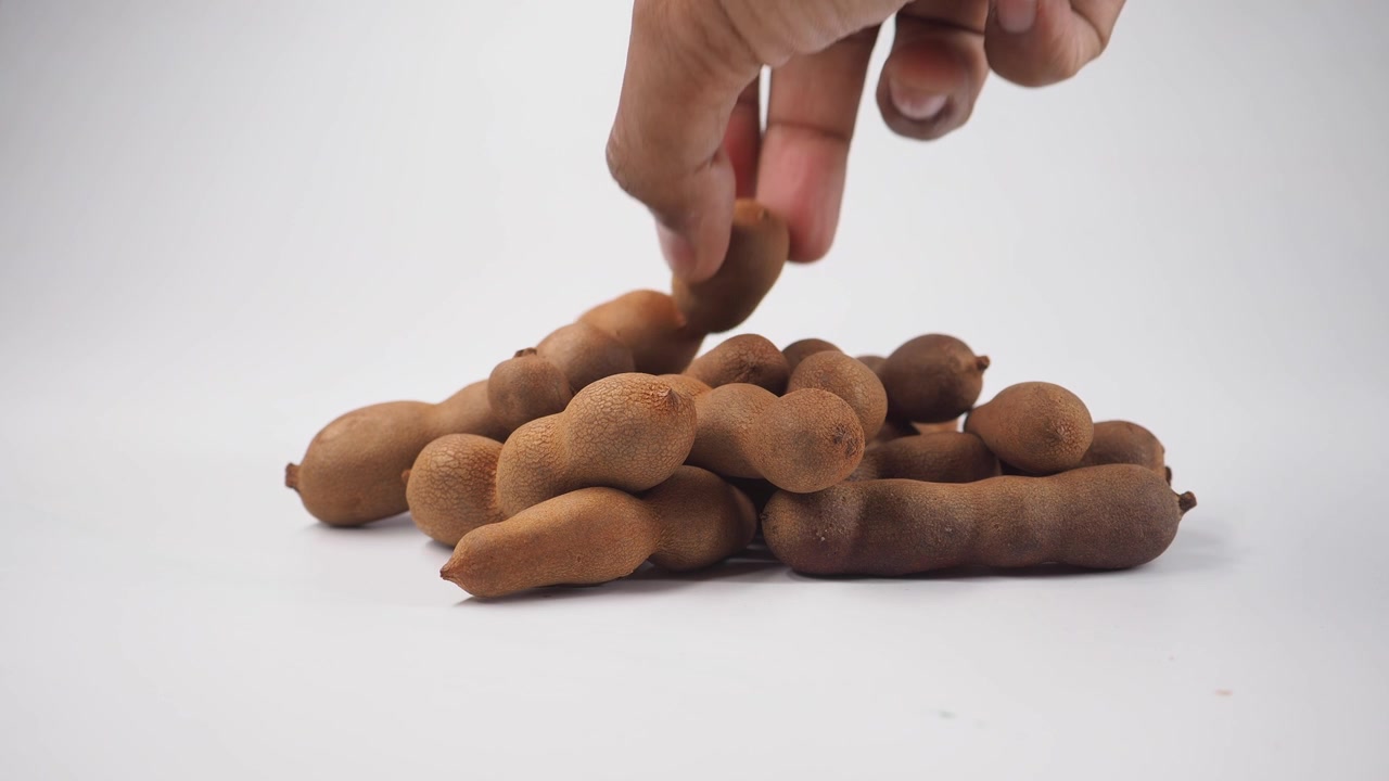 Hand Picking Fresh Tamarind Pods from a Pile on White Background