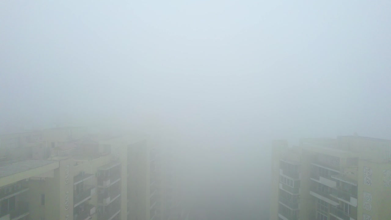 Aerial drone shot flying forward over buildings hidden in dense fog air pollution of Indian capital Delhi in severe winter prompting an emergency