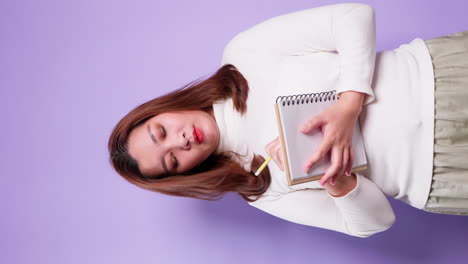 vertical of asian secretary businesswoman holding a notebook and thinking with list inspiration strategy for success on purple background