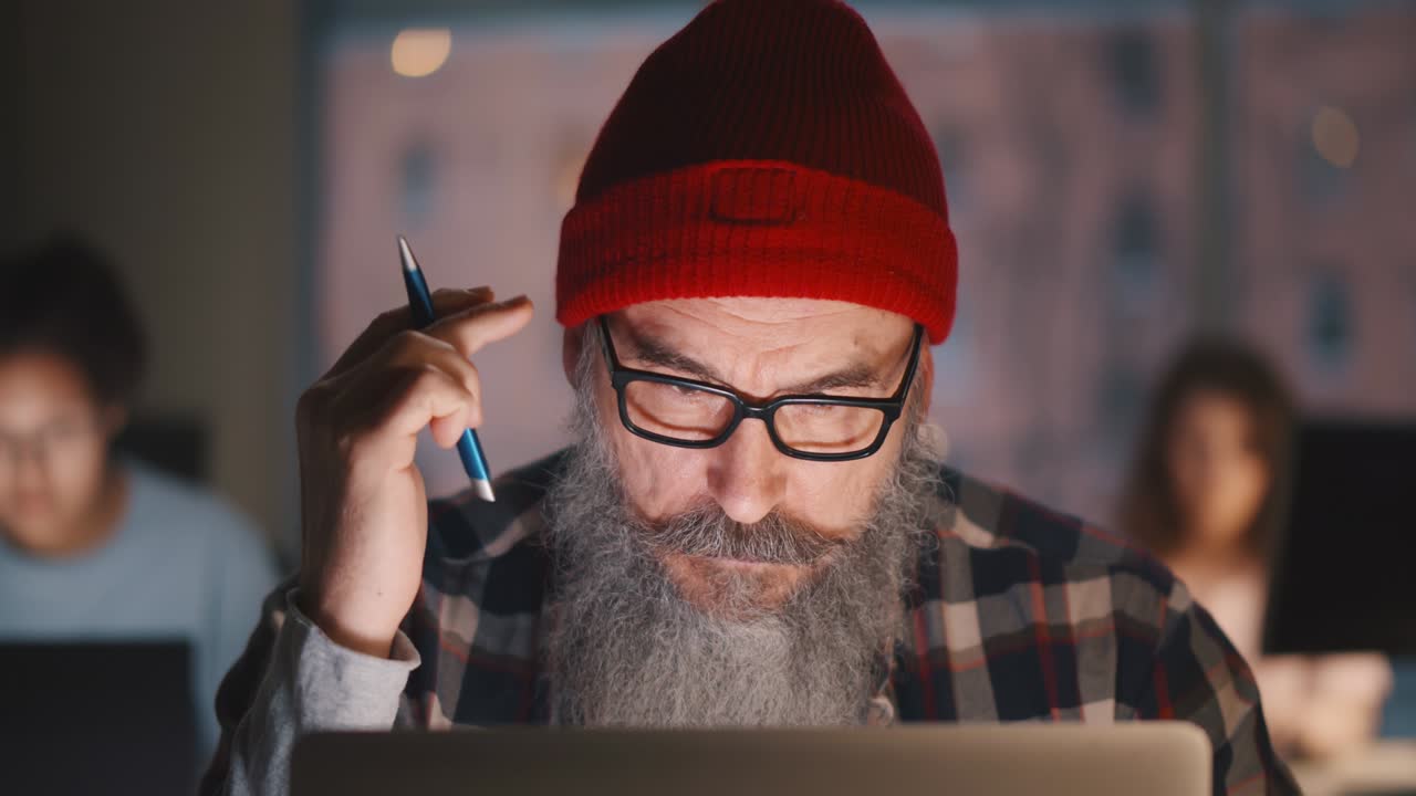 retrato de un anciano hipster barbudo sosteniendo un lápiz trabajando en una computadora portátil en la oficina
