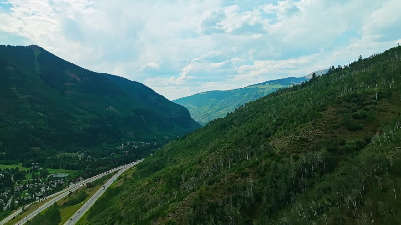 Aerial of sloping Vail hillside blanketed in vibrant green summer vegetation and trees, dolly along ridge to reveal valley